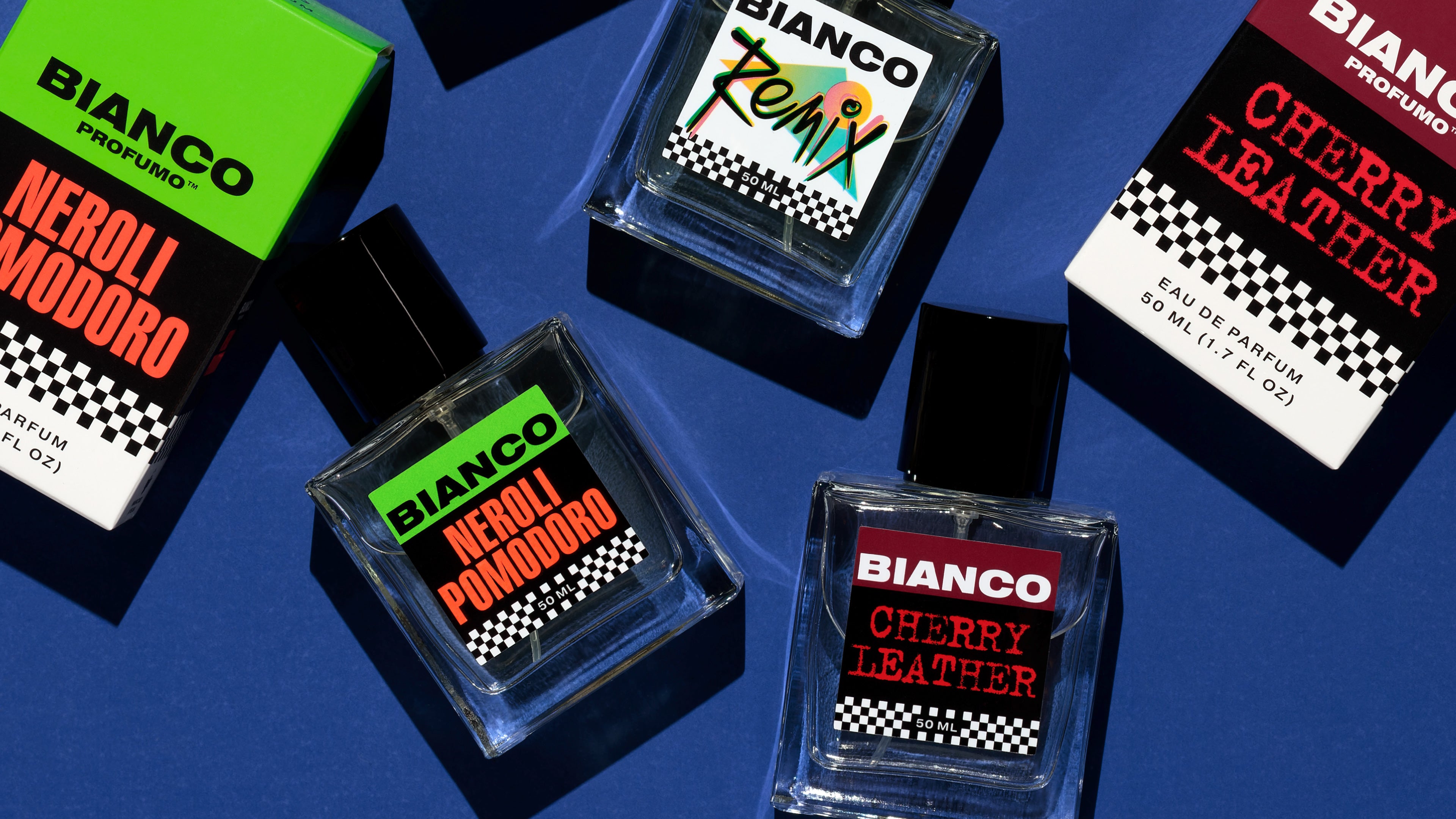 Bottles and boxes of Bianco Profumo's Remix, Neroli Pomodoro, and Cherry Leather on a deep blue background with hard lighting and deep shadows.