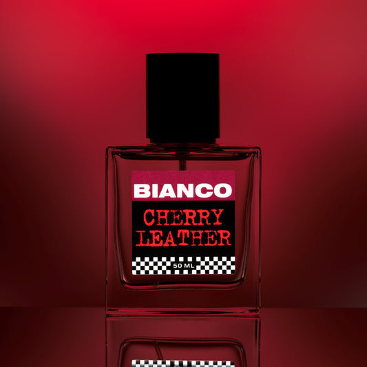 Bianco Profumo Cherry Leather with notes of Bitter Fennel, Star Anise, Black Pepper, Saffron, Ambrette Seed, Cherry, Bitter Almond, Guaiacwood, Pine Tar, Suede, Amber, Oakwood, Moss, and Musk. Bottle on a mirrored surface and red background.