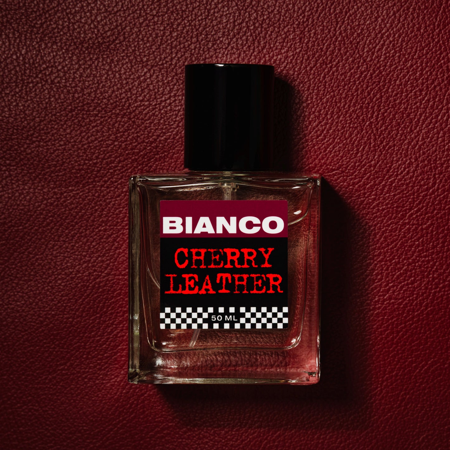 Bianco Profumo Cherry Leather with notes of Bitter Fennel, Star Anise, Black Pepper, Saffron, Ambrette Seed, Cherry, Bitter Almond, Guaiacwood, Pine Tar, Suede, Amber, Oakwood, Moss, and Musk. Bottle laid on top of a deep red piece of leather. 
