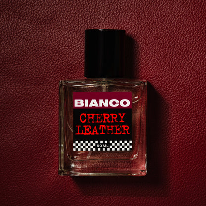 Bianco Profumo Cherry Leather with notes of Bitter Fennel, Star Anise, Black Pepper, Saffron, Ambrette Seed, Cherry, Bitter Almond, Guaiacwood, Pine Tar, Suede, Amber, Oakwood, Moss, and Musk. Bottle laid on top of a deep red piece of leather. 